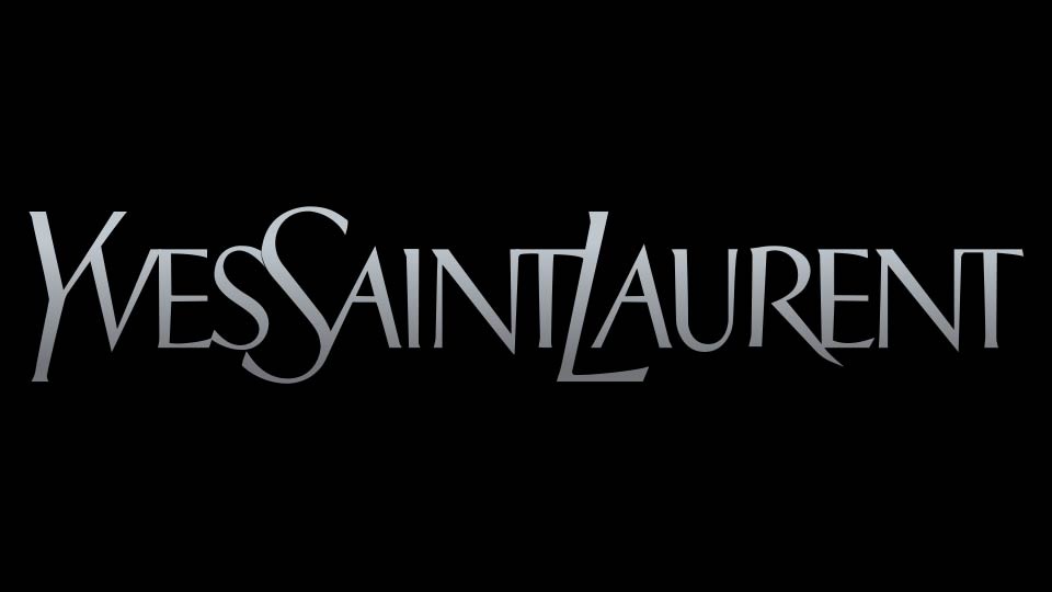The Yves Saint Laurent logo in metallic silver text on a black background, representing the classic branding designed by Cassandre in 1961